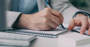 A man in a suit writing on a notebook