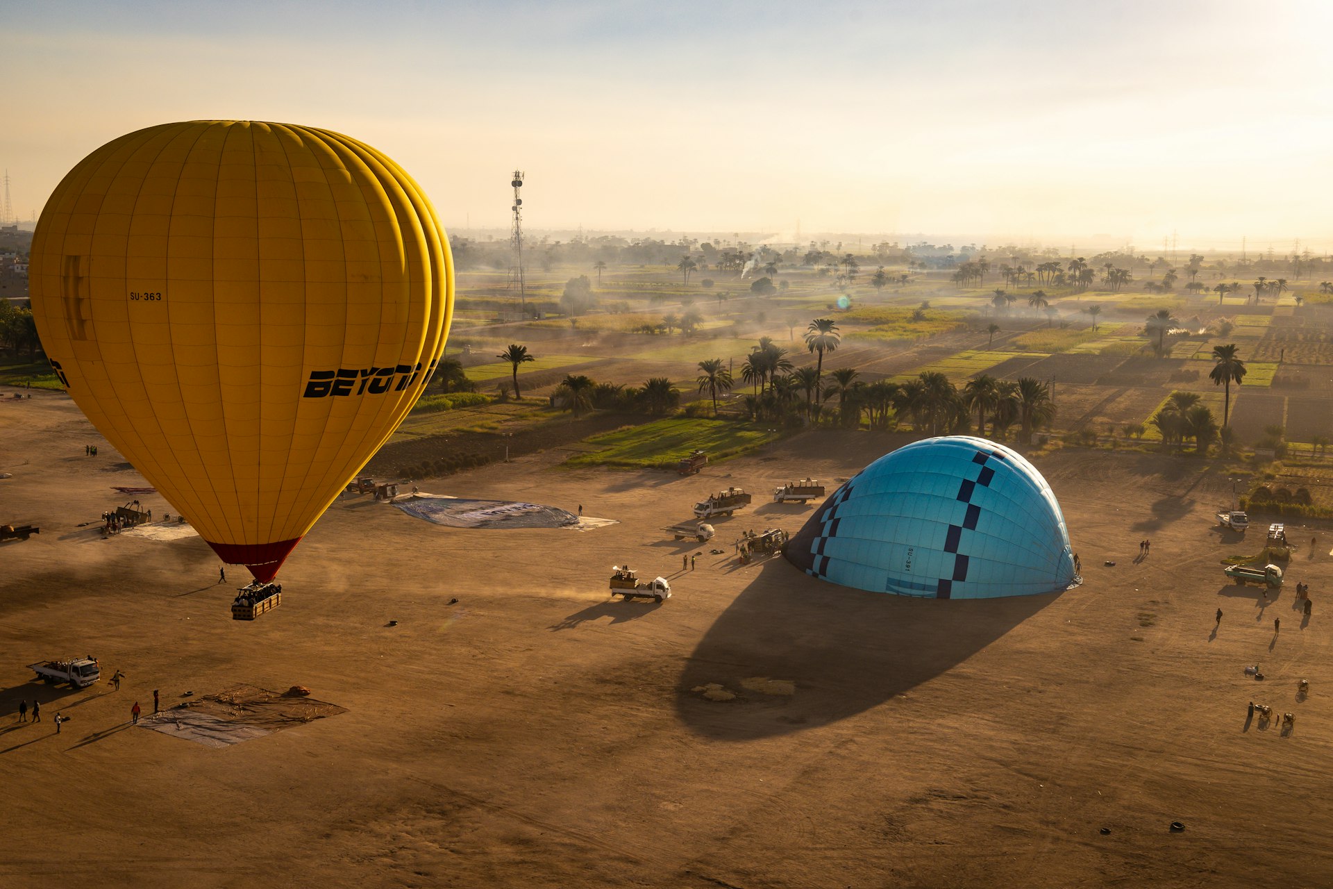 Two hot air balloons flying over a dirt field