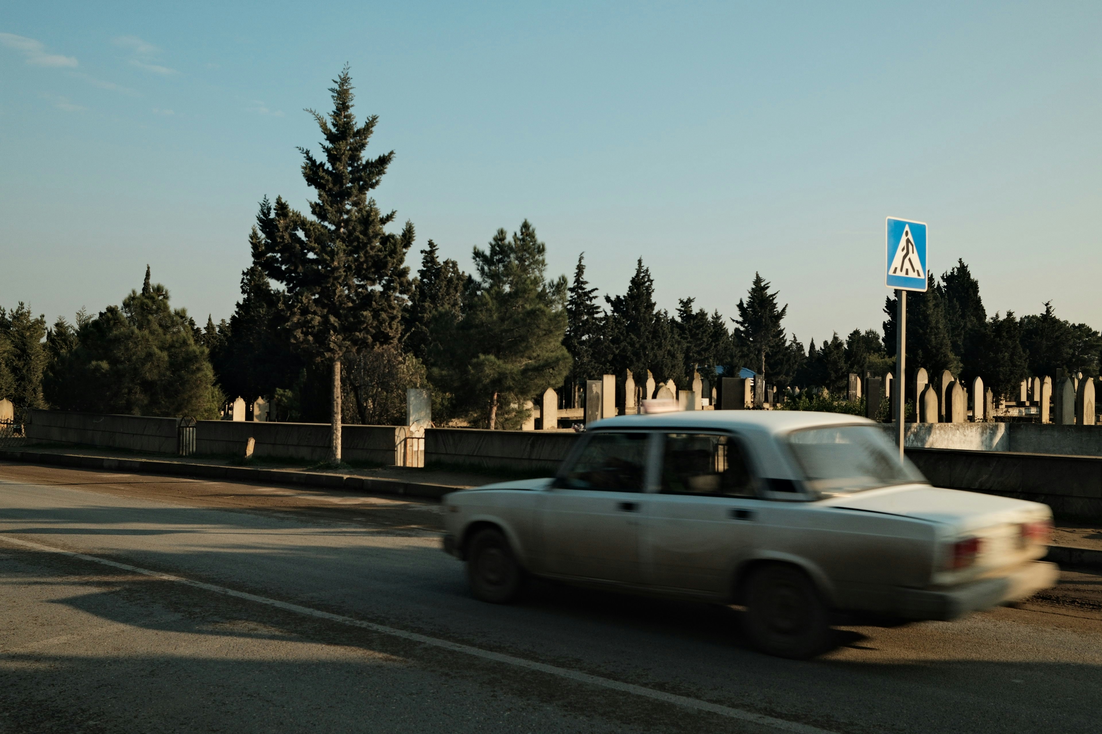 A white car driving down a street next to a forest