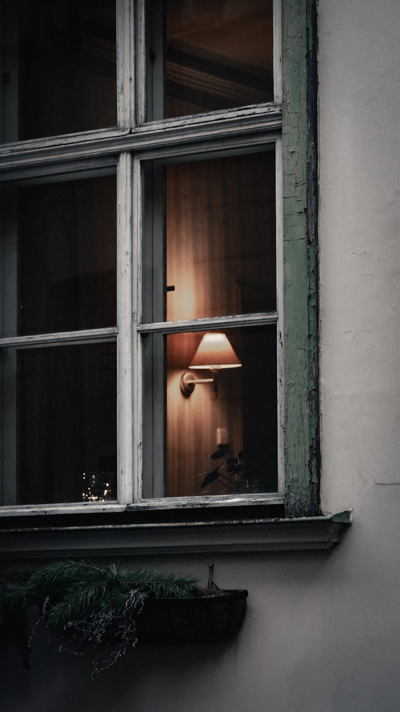 A warm amber lamp glowing on a windowsill at dusk — a feeling of sanctuary