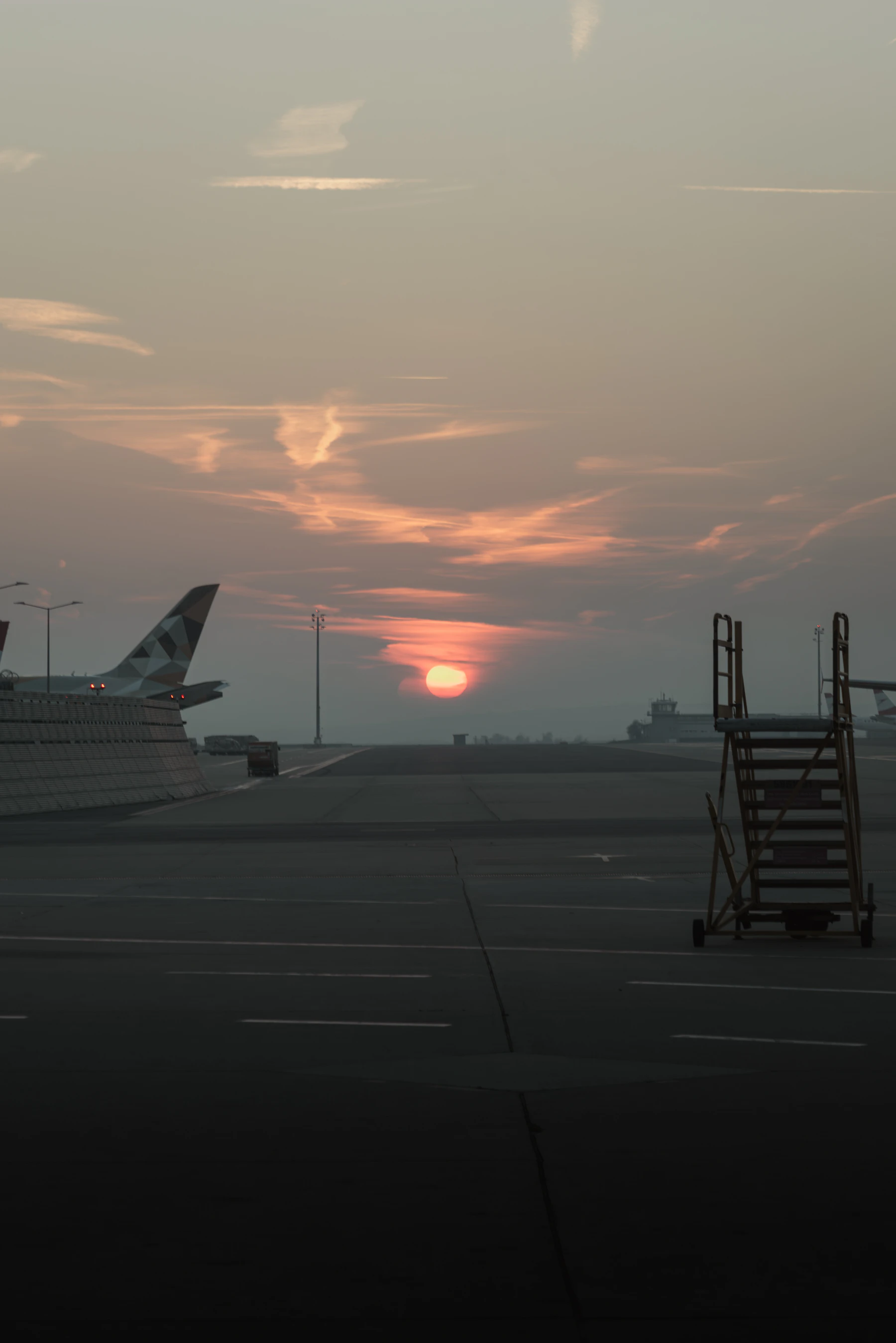 An airport apron at dusk, the sun low behind a set of boarding stairs