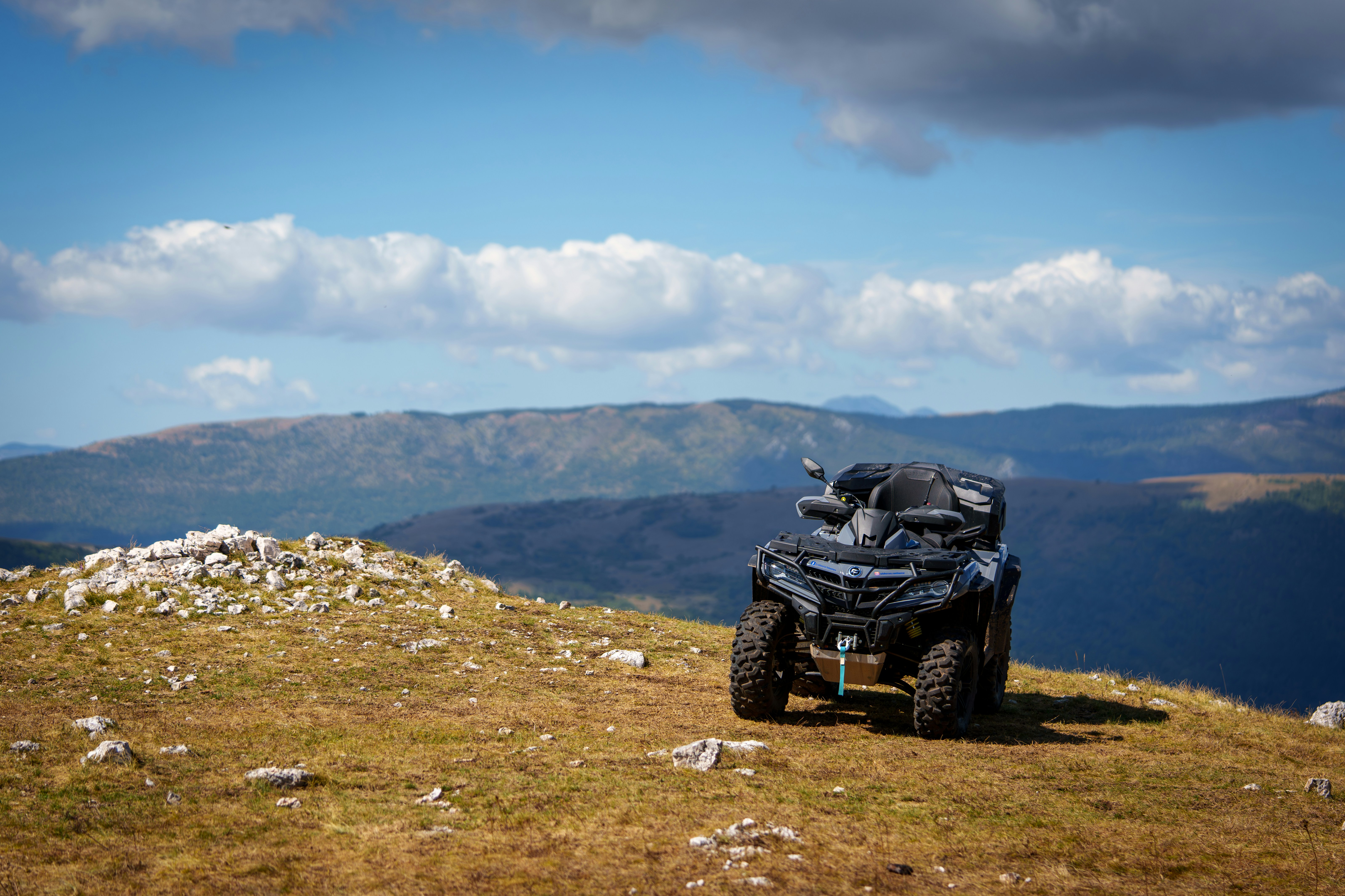 A four - wheeler on a grassy hill with mountains in the background
