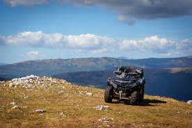 A four - wheeler on a grassy hill with mountains in the background