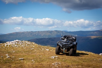 A four - wheeler on a grassy hill with mountains in the background