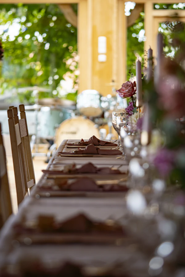 A long dinner table set with napkins and flowers under a timber pergola