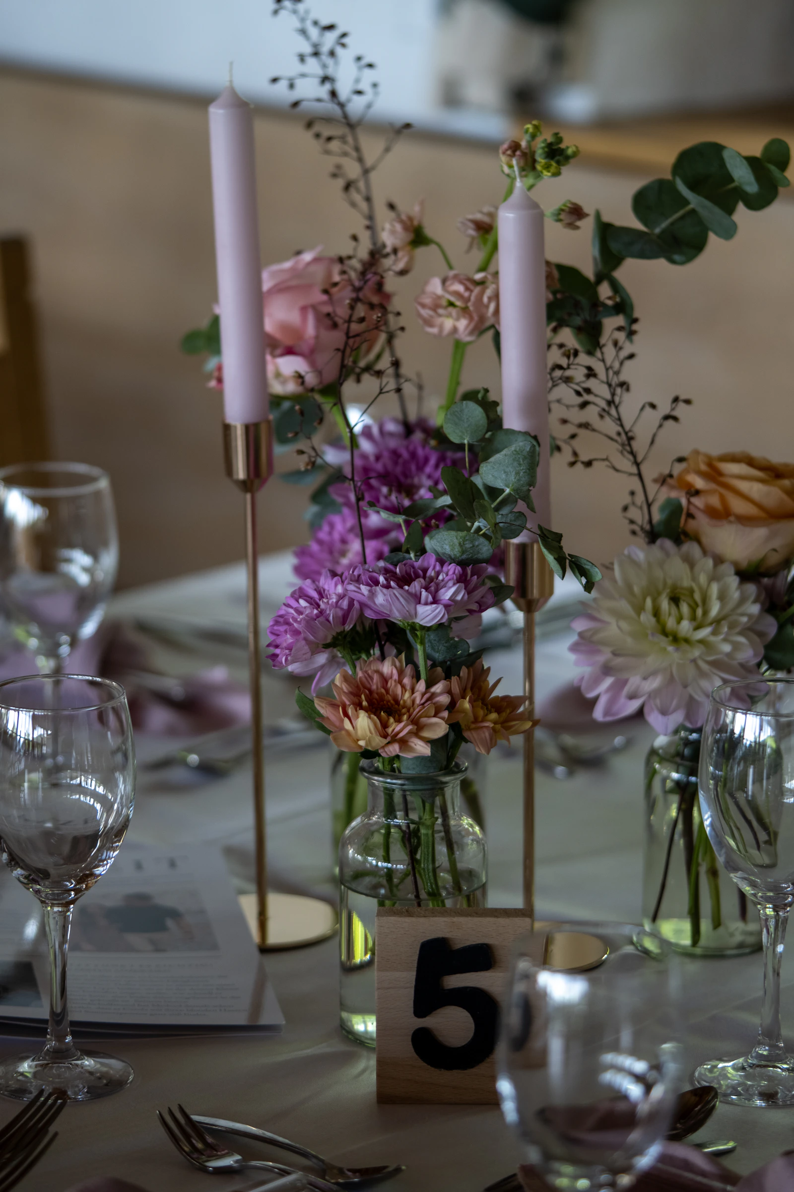 Pink flowers, eucalyptus and taper candles on a reception table.