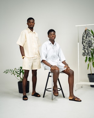 Two men sitting on stools in front of a white background
