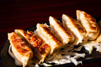 A black plate topped with dumplings on top of a wooden table