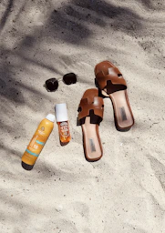 A pair of sandals and a bottle of sunscreen on a beach