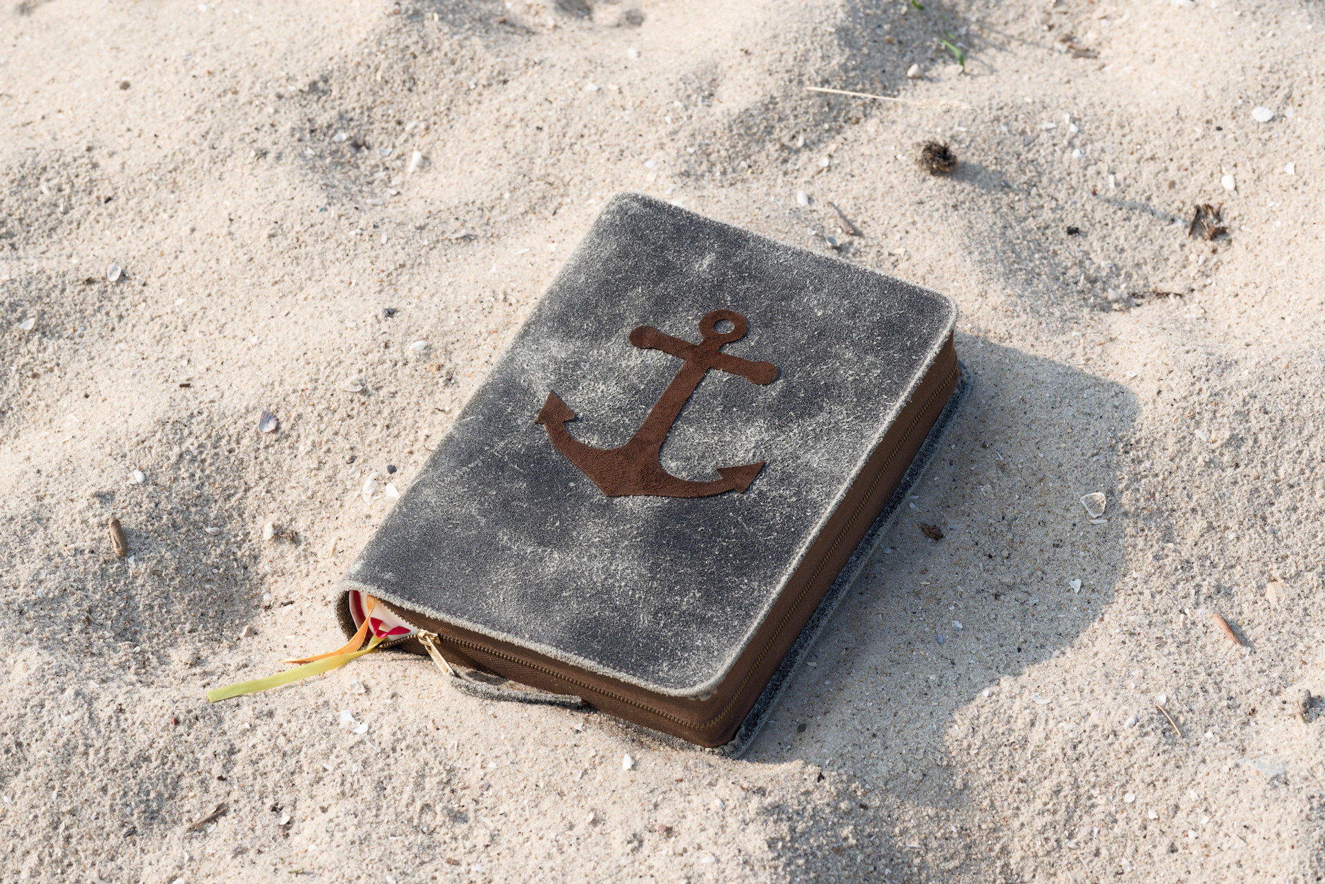 A book with an anchor on it laying in the sand