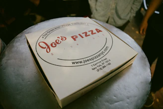 A pizza box sitting on top of a white pillow