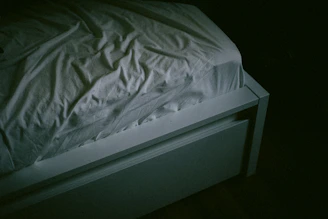 A bed with a white comforter in a dark room