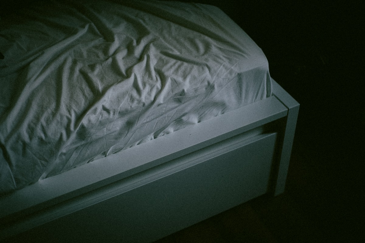A bed with a white comforter in a dark room, evoking restless disrupted sleep