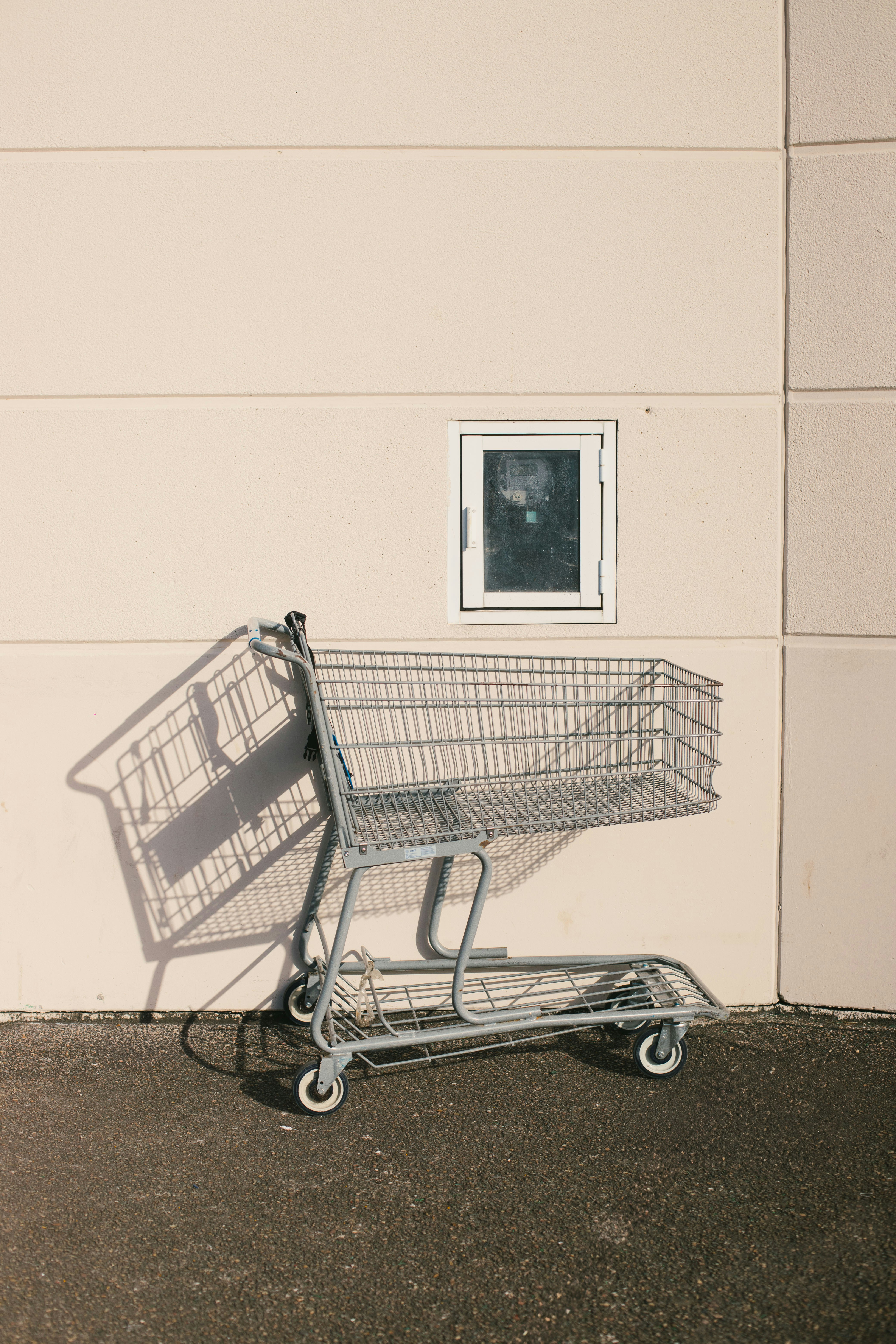 Shopping cart casts a long shadow against wall.