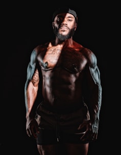 A man with a beard and no shirt standing in the dark