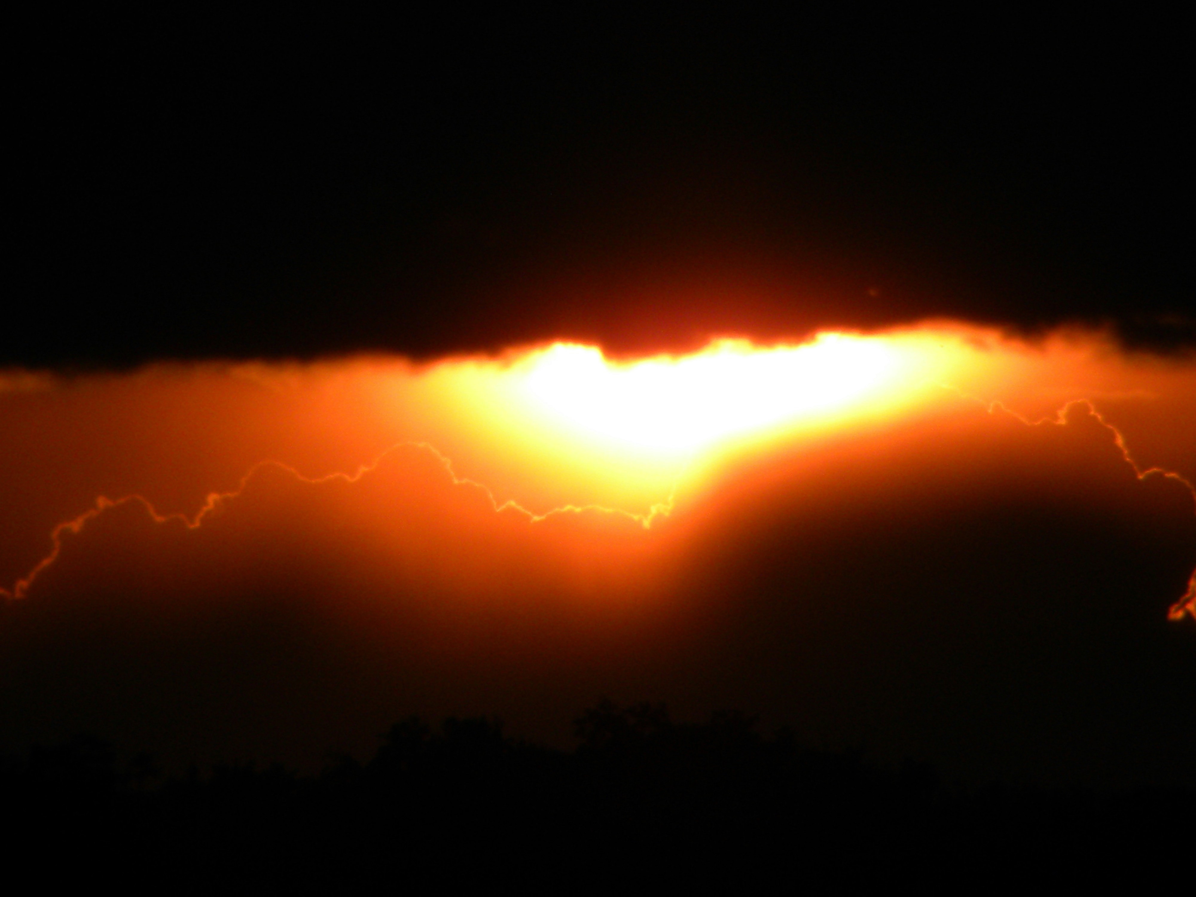 The sun is setting behind a cloud in the sky