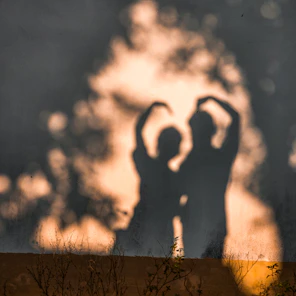A shadow of two people standing in front of a tree making a heart shape with their arms