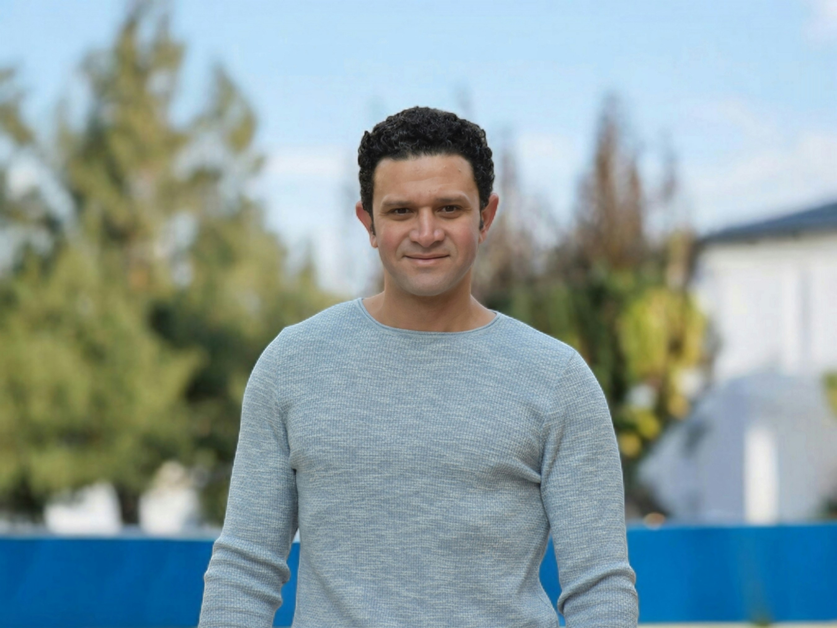 A man in a gray sweater holding a tennis racquet
