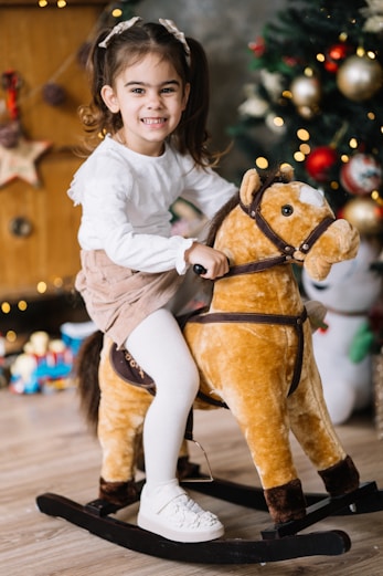 A little girl riding a rocking horse in front of a christmas tree