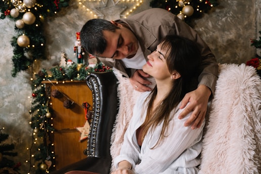 A man and woman sitting on a couch in front of a christmas tree