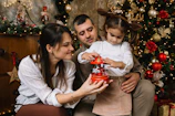 A man and a woman holding a baby in front of a christmas tree