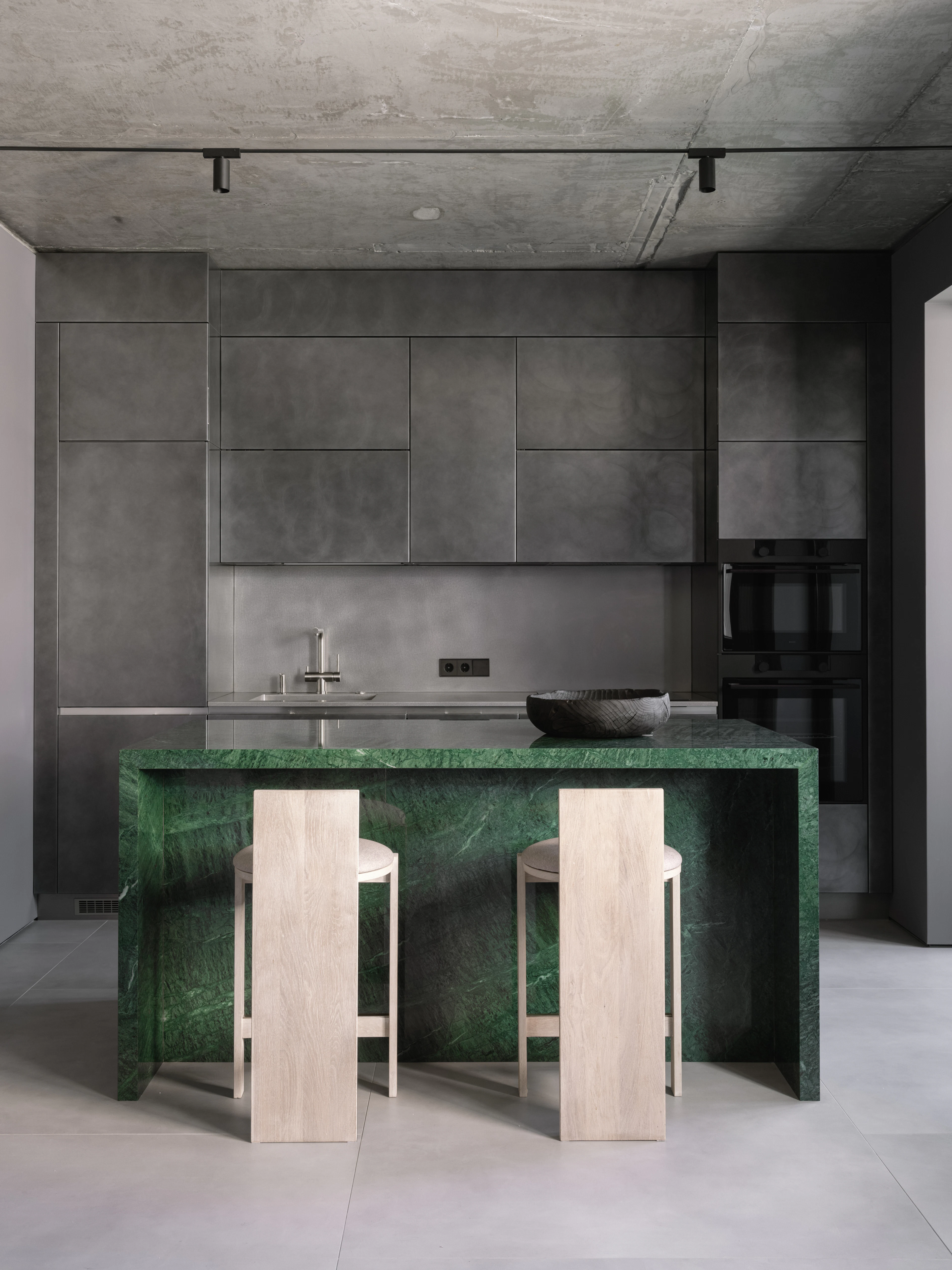 Kitchen with a green marble island, pale oak stools and concrete-grey cabinetry