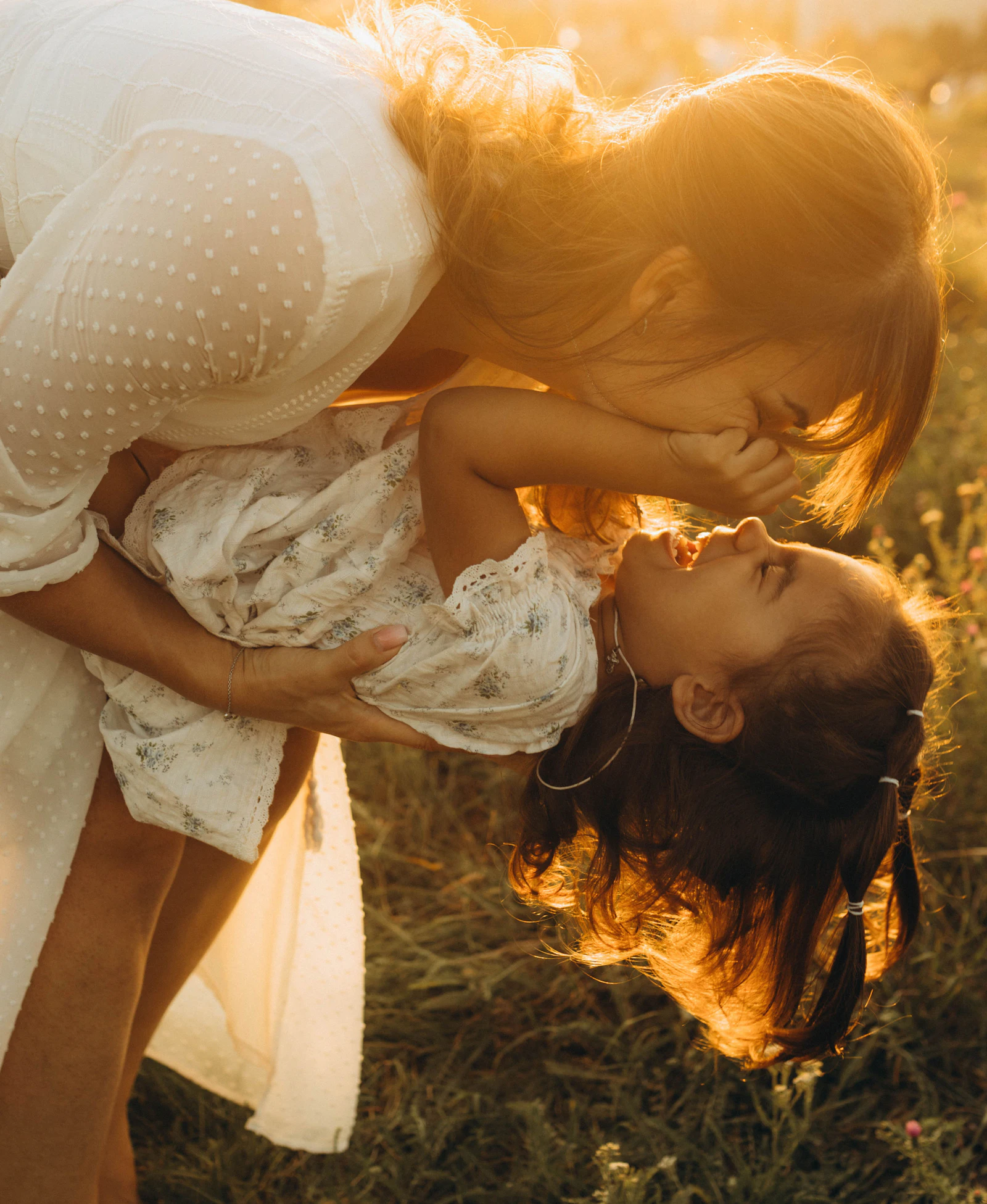 A mother and her young daughter laughing together in warm evening light