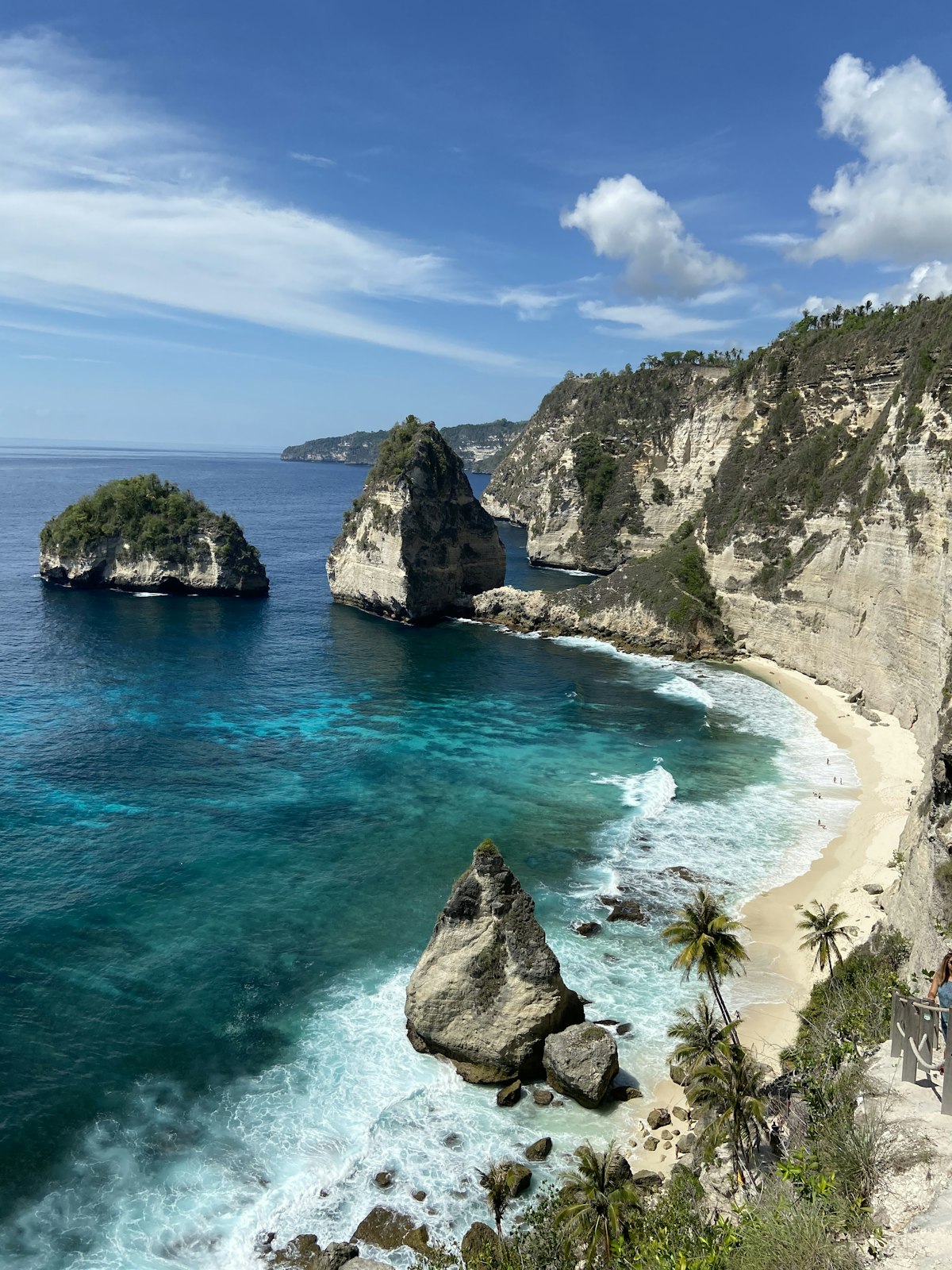 A sandy beach with blue water next to a cliff in Nusa Penida