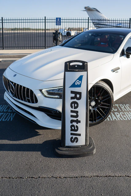 A white car parked next to a car rental sign