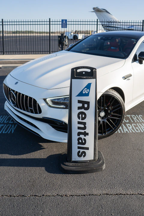 A white car parked next to a car rental sign
