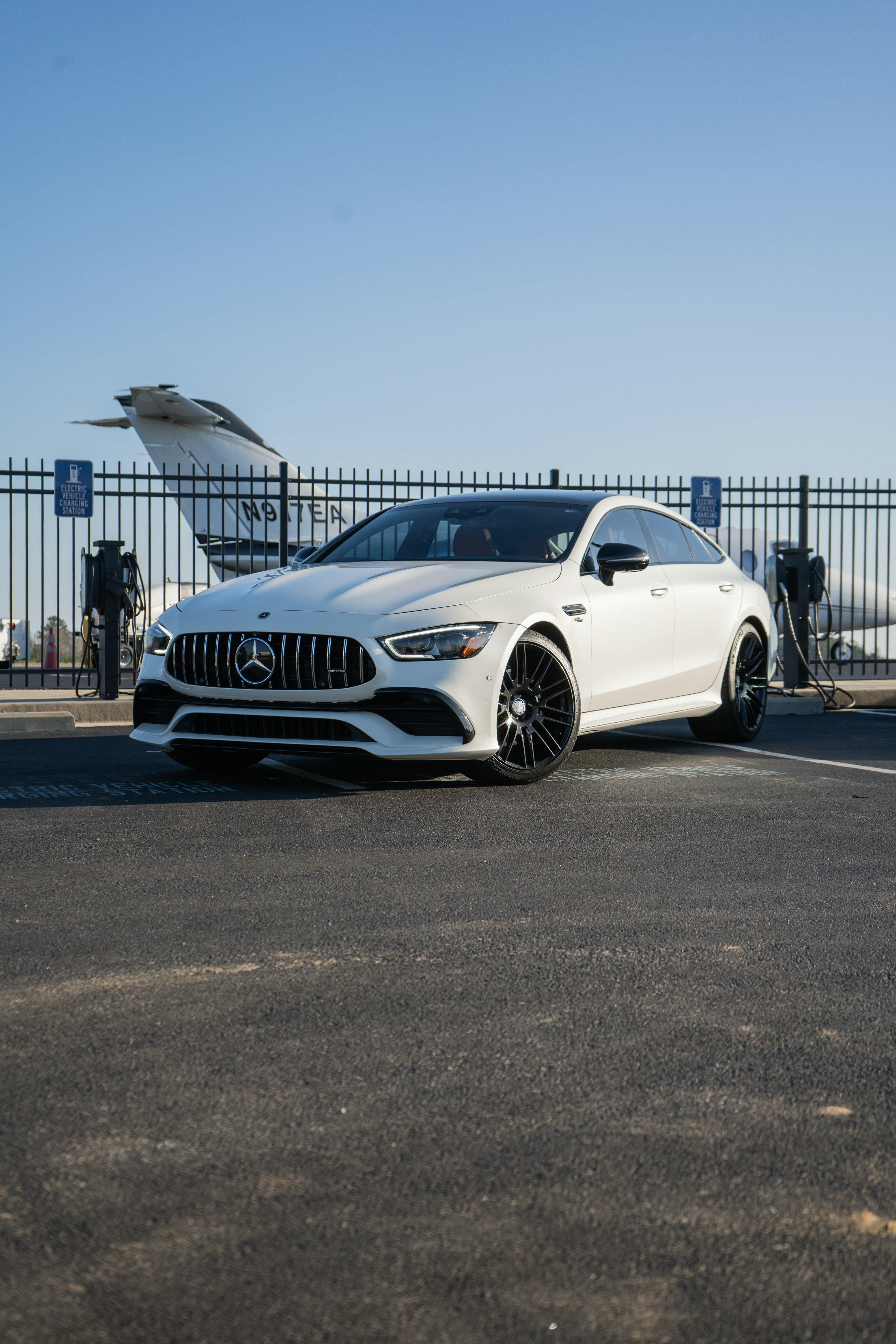 White luxury sedan parked by a private jet and charging stations.