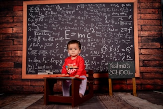 A little boy sitting at a desk in front of a chalkboard