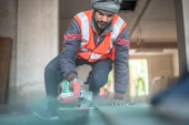 A man in an orange vest is working on a piece of metal