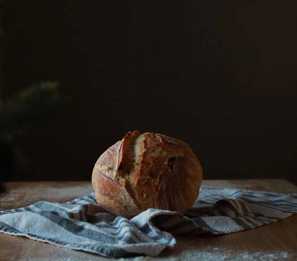 Freshly baked loaf of bread rests on blue and white striped cloth on table