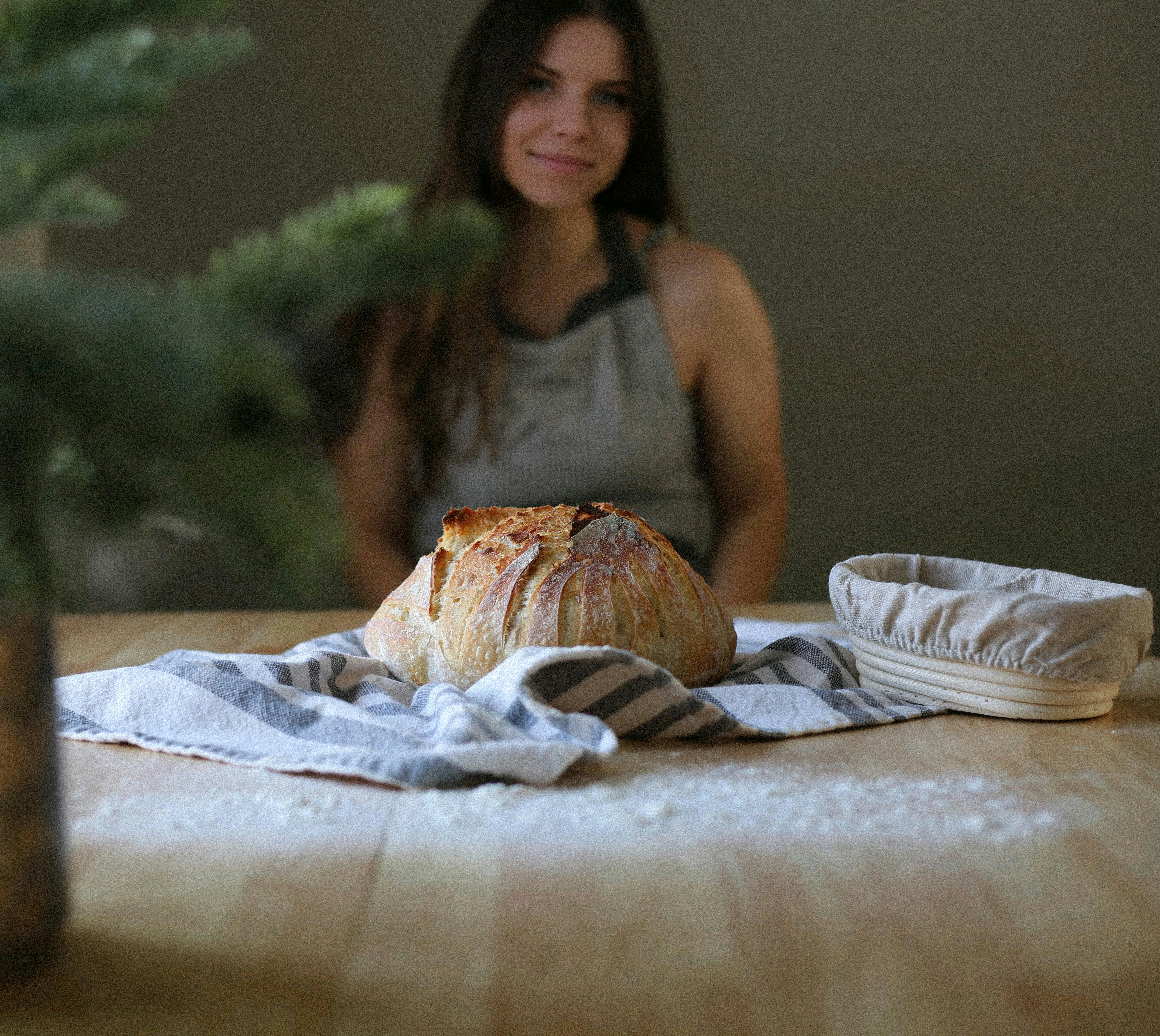 A woman sitting at a table with a loaf of bread