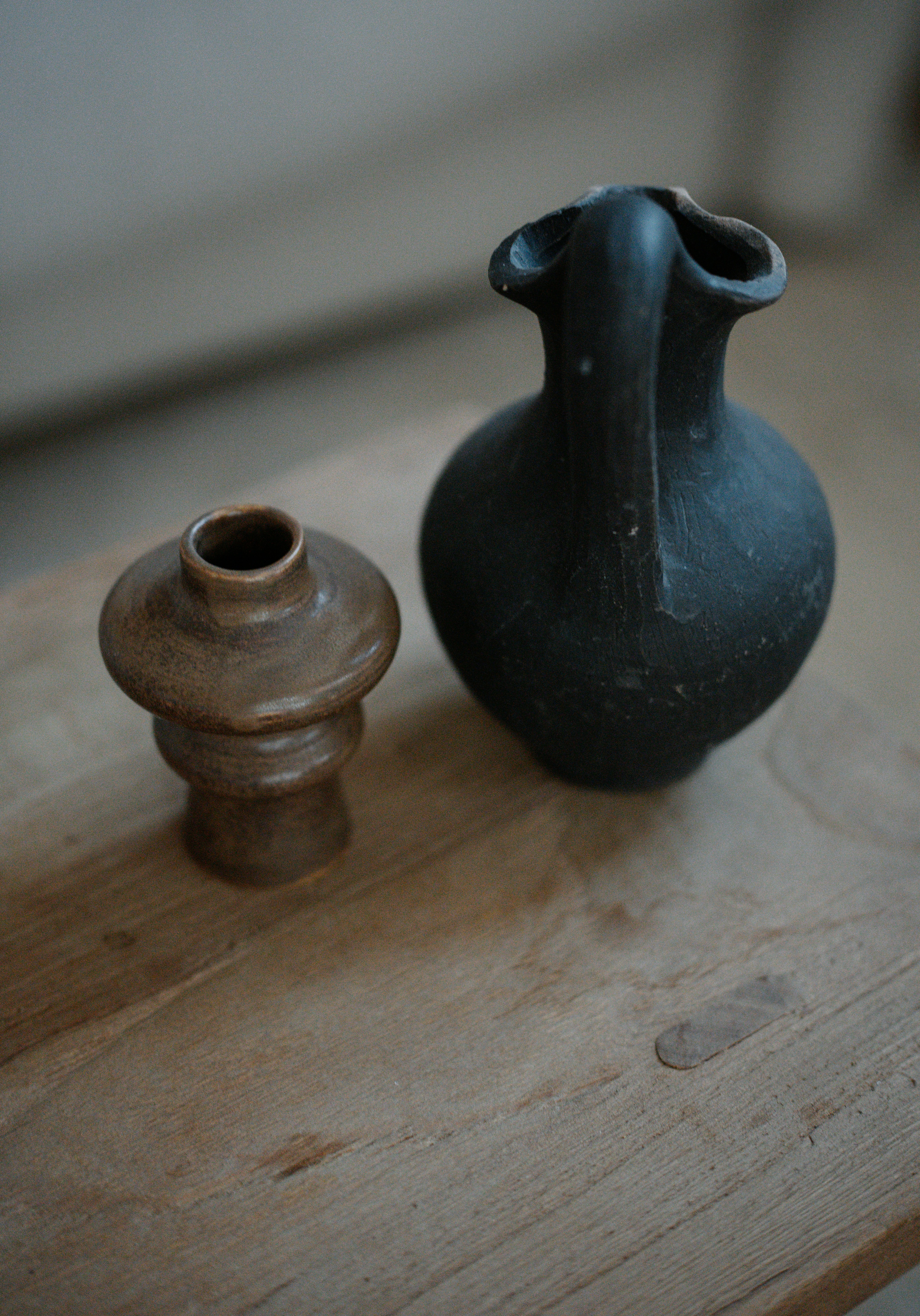 A black vase sitting next to a brown vase on a wooden table