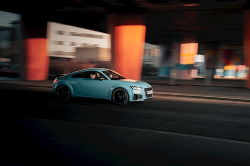A blue car driving down a street next to tall buildings