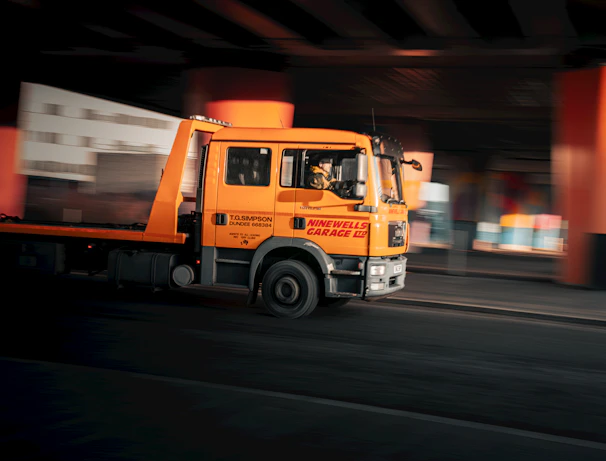 A yellow truck driving down a street under a bridge
