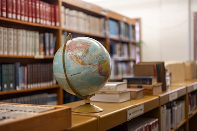 A globe sitting on top of a book shelf in a library