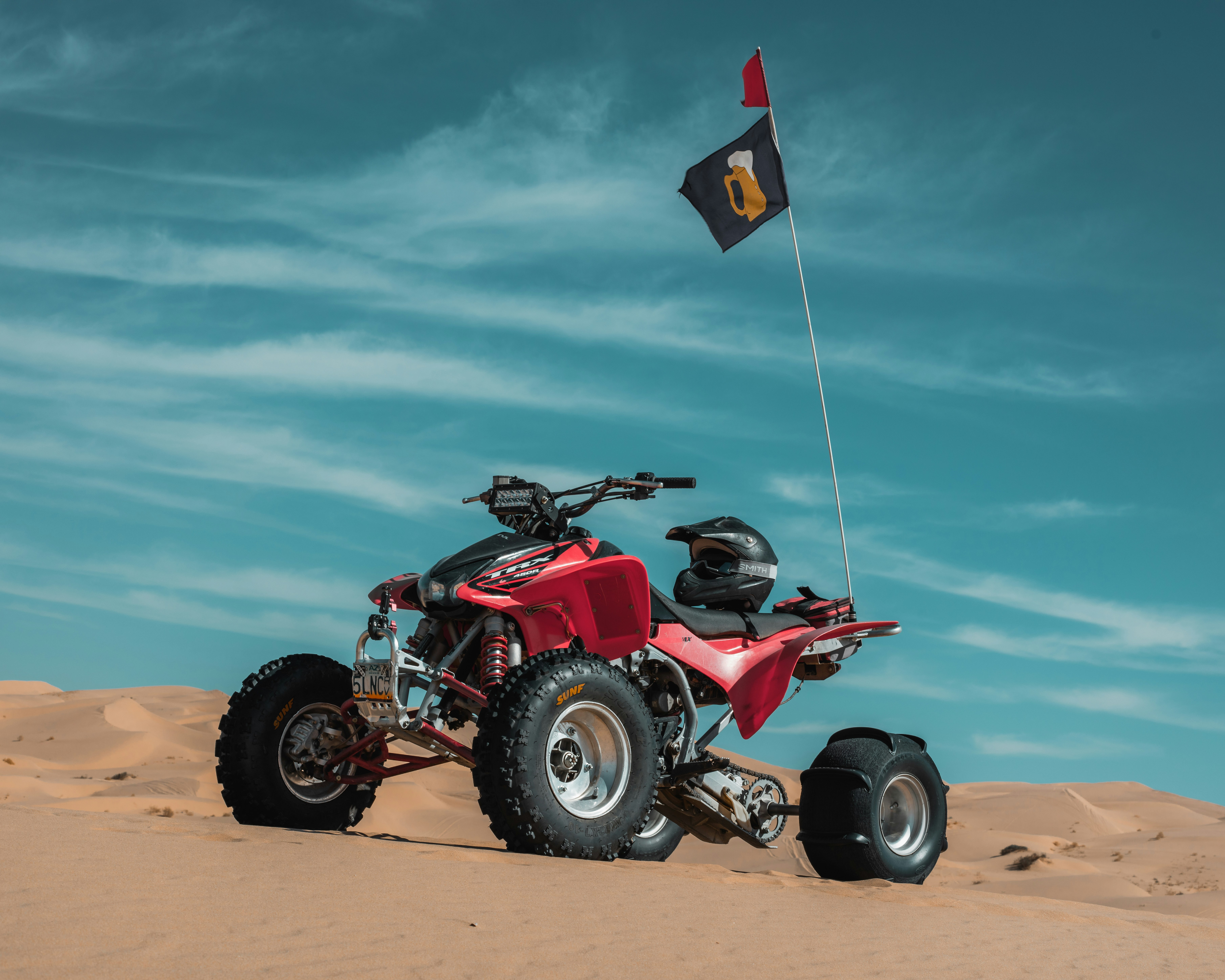 A red four wheeler in the desert with a flag