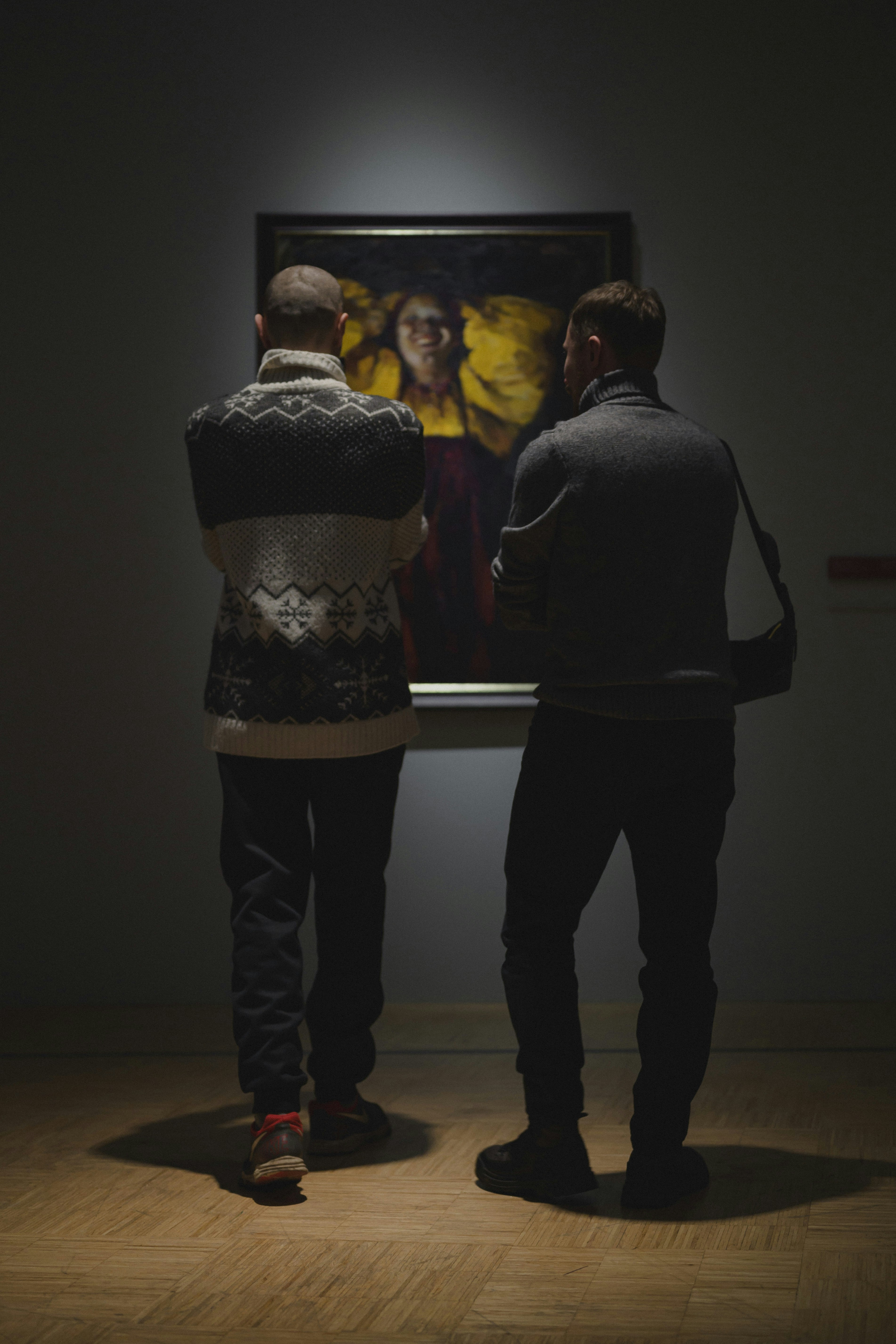 Two people looking at a painting in a dark room