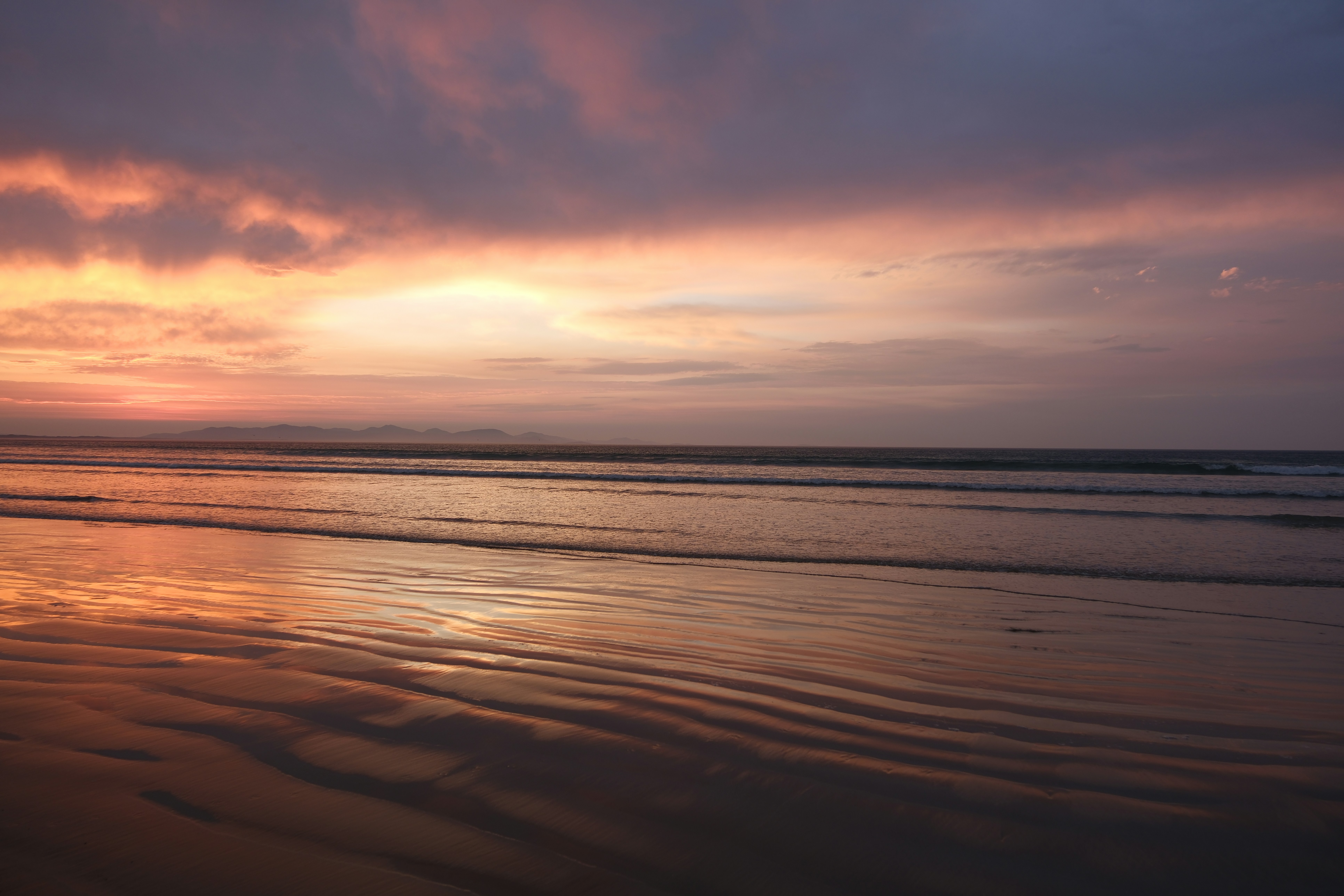 The sun is setting over the water at the beach