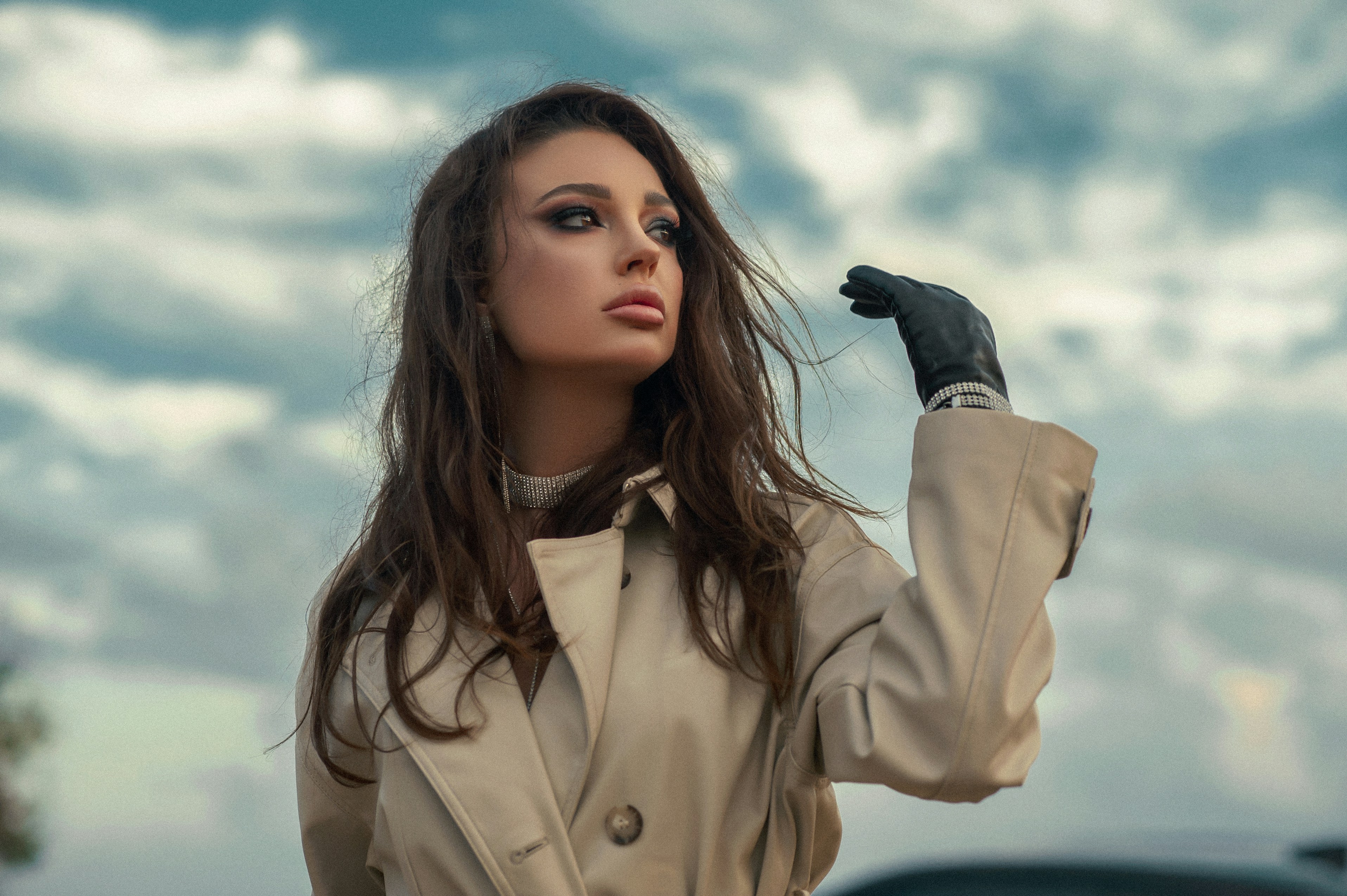 A woman in a beige trench coat under a cloudy sky
