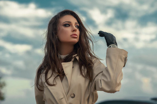 A woman in a beige trench coat under a cloudy sky