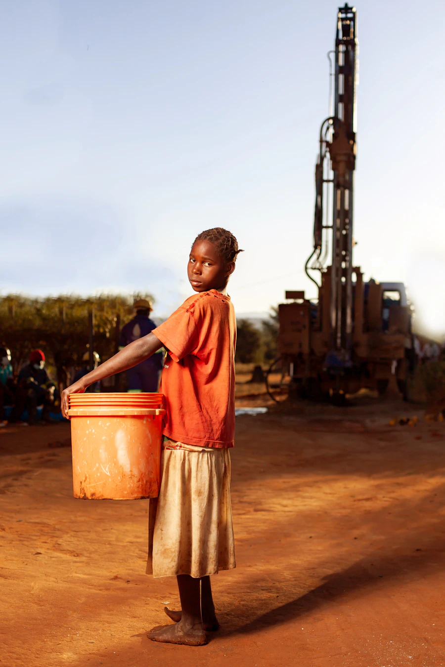 A boy carrying water beside a well-drilling rig