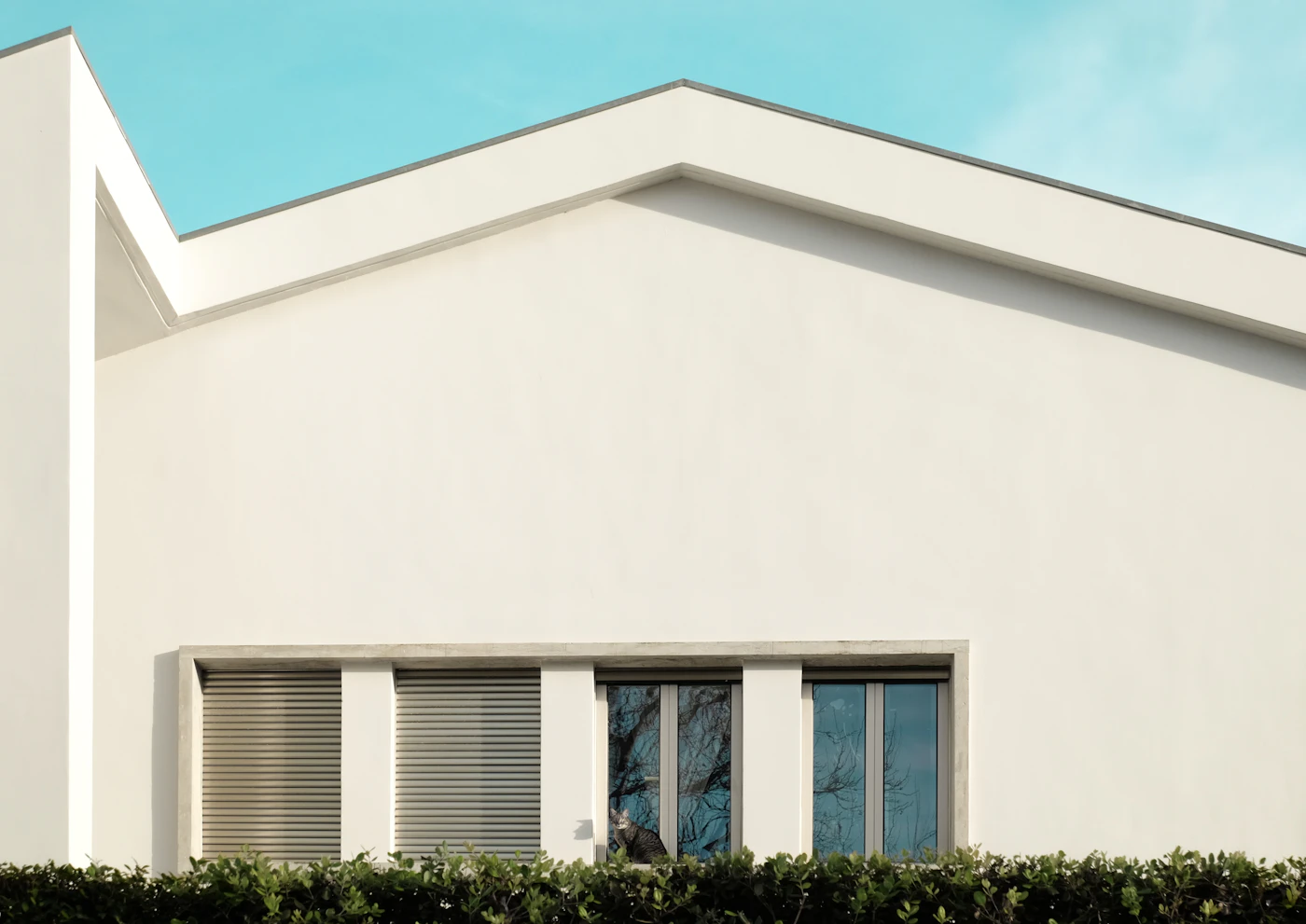 A white modern house behind a trimmed hedge