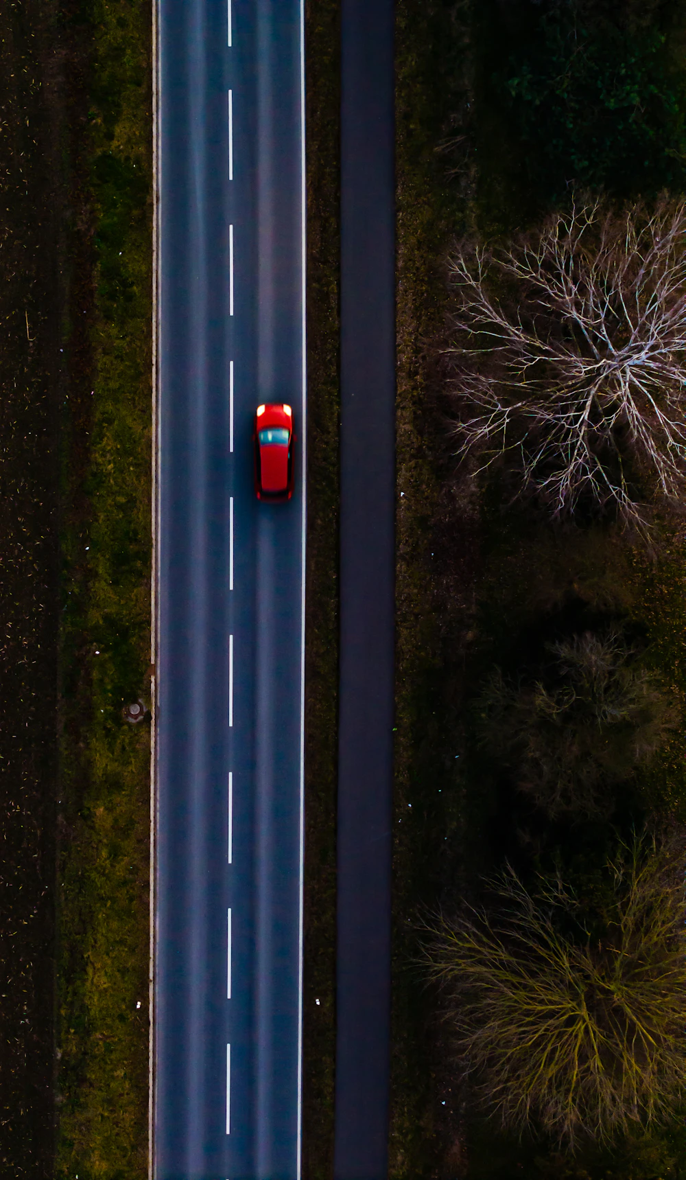 Aerial view of a single car travelling along a tree-lined road in Germany