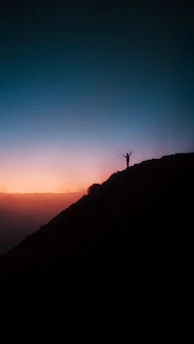 A person standing on top of a hill at sunset