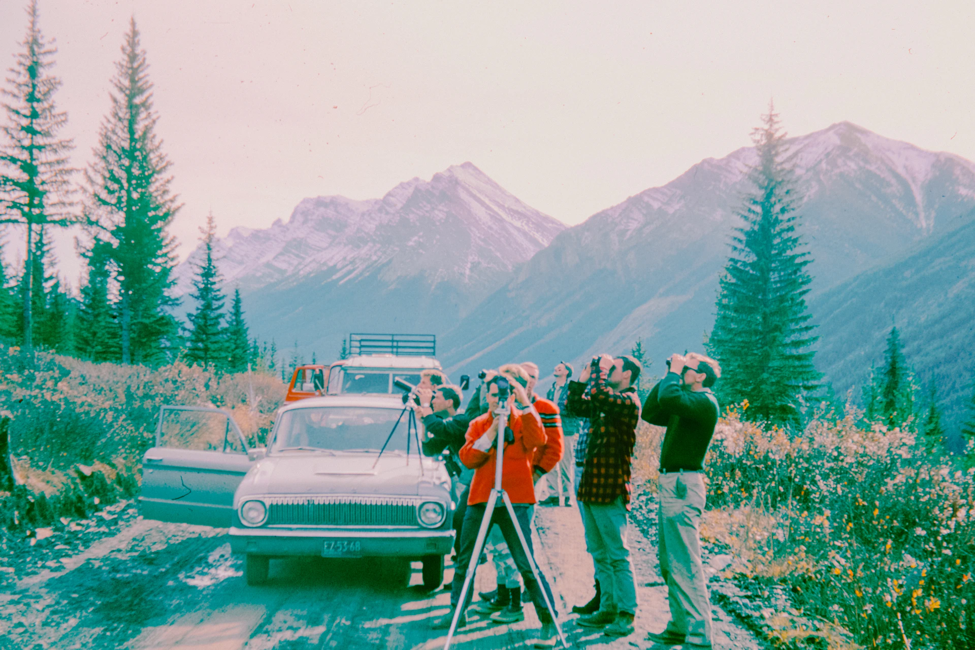A group of people standing next to a car on a dirt road