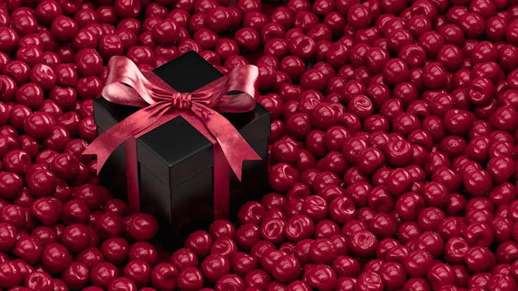 A black box with a red bow on top of a pile of red balls